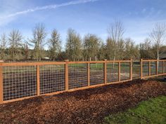 a wooden fence with wire on top and grass in the middle, next to a dirt field