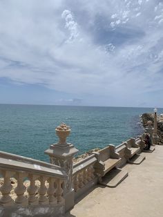 a person sitting on a bench looking out at the ocean from a balcony with railings