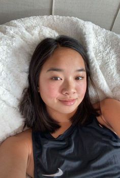 a young woman laying on top of a bed next to a white comforter and pillow