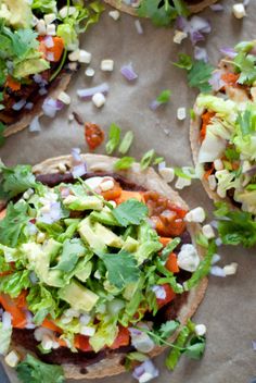 three tacos with lettuce, tomatoes and other toppings on paper wrappers