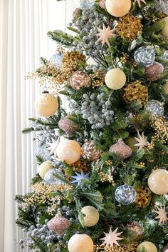 a christmas tree decorated with ornaments and greenery in gold, silver and white colors