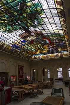 the inside of a building with many tables and benches under a colorful glass ceiling above