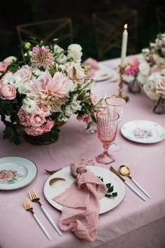 the table is set with pink and white plates, silverware, and floral centerpieces