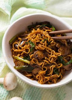 a bowl filled with noodles and mushrooms on top of a green towel next to two chopsticks