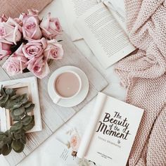 a cup of coffee and some pink roses on a table next to an open book