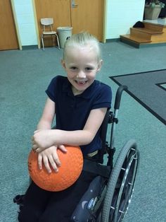 a young boy in a wheelchair holding an orange ball