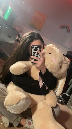 a woman taking a selfie with her cell phone while holding a large teddy bear