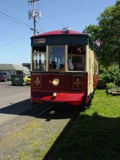 a red and yellow trolley car traveling down train tracks next to a lush green field