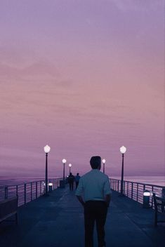 a man standing on top of a pier next to the ocean at night with street lights