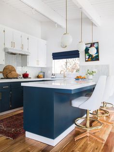 a kitchen with blue cabinets and white counter tops, gold bar stools and an area rug