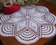 a white doily sitting on top of a wooden table next to a red pillow