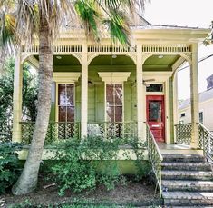 a yellow house with red door and steps leading up to the front porch, surrounded by palm trees