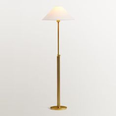 a gold floor lamp with a white shade on the top and bottom, standing against a wall