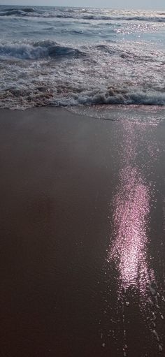 the sun is shining on the sand at the ocean's edge as waves roll in