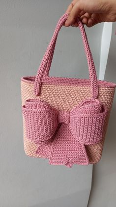 a hand holding a pink knitted purse with two bows on the front and side