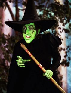 a woman dressed in green and black holding a wooden stick while wearing a witch costume