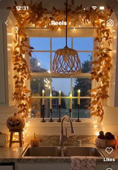 a kitchen sink under a window covered in fall leaves and pumpkins next to a lit candle