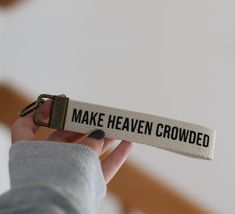 a person holding up a keychain that says make heaven crowded in black and white