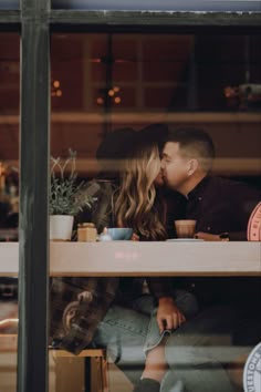 a man and woman kissing while sitting at a table in front of a store window