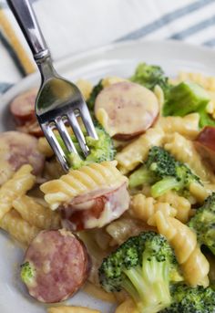 a white plate topped with pasta and broccoli next to a fork in it