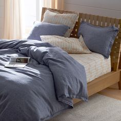 a bed with blue sheets and pillows in a bedroom next to a wooden headboard