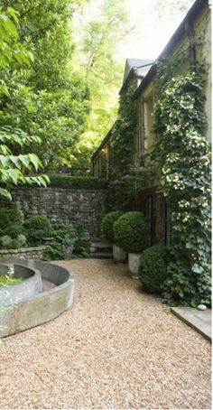 an outdoor garden with stone walls and gravel path leading up to the house, surrounded by greenery