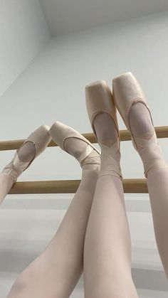 three ballet feet in the air with their bare legs on a wooden rail above them