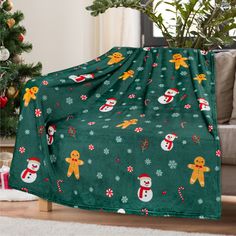 a green christmas blanket with snowmen and gingerbreads on it next to a christmas tree