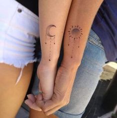 two girls with matching tattoos on their arms holding hands, one has the sun and the other has the moon