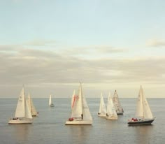 several sailboats are sailing in the ocean on a cloudy day with no one around them