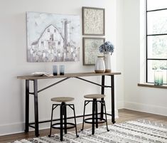 two stools sit in front of a table with a laptop on it and a painting hanging above