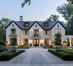 a large white brick house with lots of windows and bushes in front of the entrance