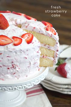 a strawberry cake with white frosting and fresh strawberries on the top is ready to be eaten