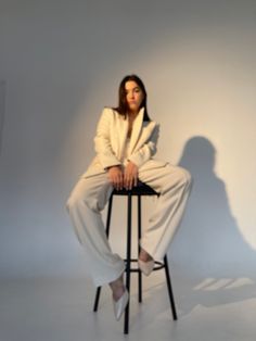 a woman sitting on top of a stool in front of a white wall and shadow