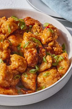 a white bowl filled with fried chicken and garnished with green leaves on top