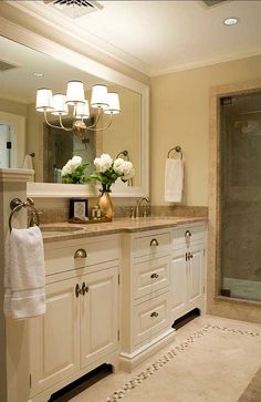 a large bathroom with white cabinets and marble counter tops, an open shower stall and a chandelier