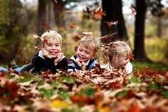 three young children laying on the ground surrounded by leaves