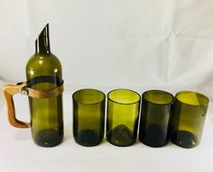 a set of four green glass cups and a wine bottle with a wooden handle sitting next to each other