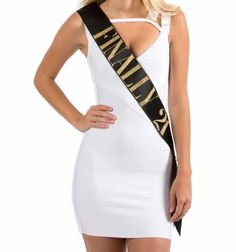 a woman in a white dress with a black and gold sash around her neck is posing for the camera