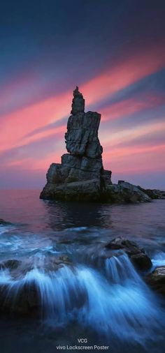 a rock formation sitting on top of a rocky beach next to the ocean at sunset