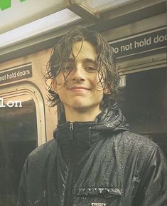 a man with wet hair standing in front of a subway train door and looking at the camera