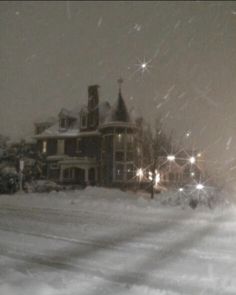 a snow covered street with a large building in the background and lights shining on it