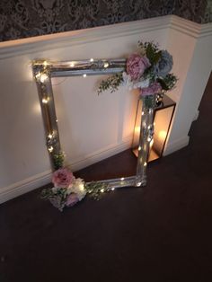 a mirror frame with flowers and lights on the floor next to a candlelight holder