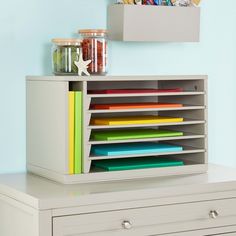 a white dresser with many different colored folders on the top and bottom drawers in front of it