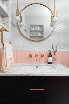 a bathroom with pink and white tile, gold fixtures and a round mirror above the sink