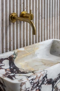 a marble sink with gold faucet and wall mounted soap dispenser