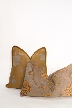 two pillows sitting next to each other on top of a white surface with yellow and brown flowers