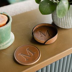 two leather coasters sitting on top of a table next to a potted plant