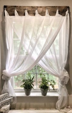 a window with white curtains and potted plants