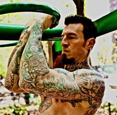 a man with tattoos on his arms and chest is holding a green object above his head